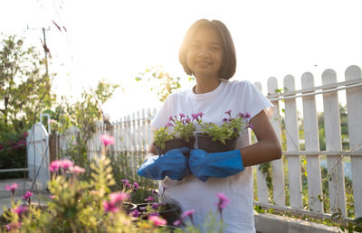 Woman standing by flowering plants against fence