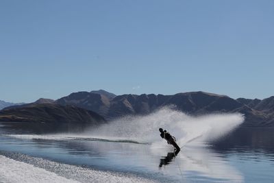 Man surfing in water against clear blue sky