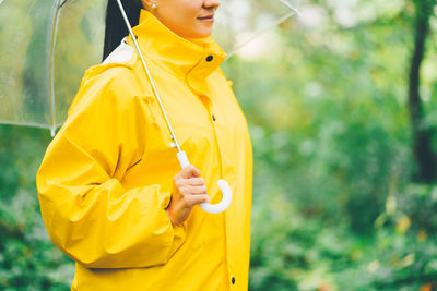 Midsection of woman in raincoat with umbrella standing outdoors