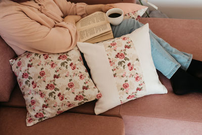 Low section of woman reading book sitting on sofa at home