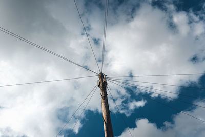 Low angle view of electricity pylon against cloudy sky