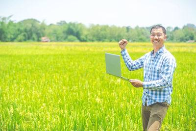 Portrait of smiling young man using laptop on field