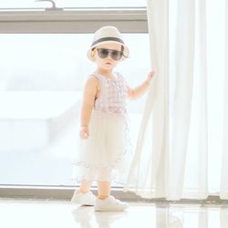 Portrait of baby girl standing by window at home