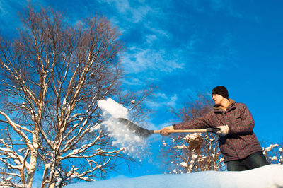 Low angle view of man shoveling snow against blue sky
