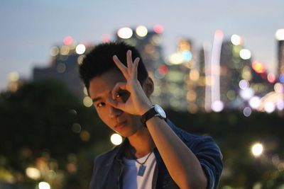 Portrait of young man gesturing against city lights at night