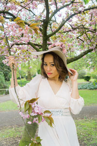 Beautiful young woman standing by tree in park