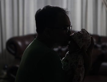Side view of father kissing newborn daughter while sitting at home