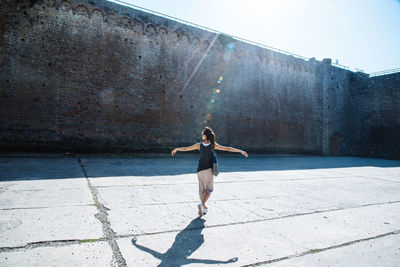 Rear view of woman standing with arms outstretched against wall