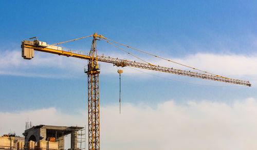 Low angle view of cranes at construction site against sky