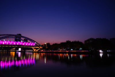 Illuminated bridge over lake against blue sky at night