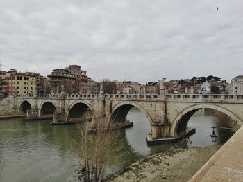 Arch bridge over river against sky in city