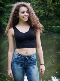 Happy young woman standing by lake at park