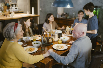 Smiling senior couple holding hands while having dinner with family at home