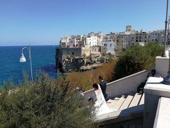 Buildings by sea against clear blue sky