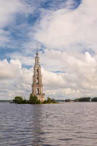 Tower of building by river against cloudy sky