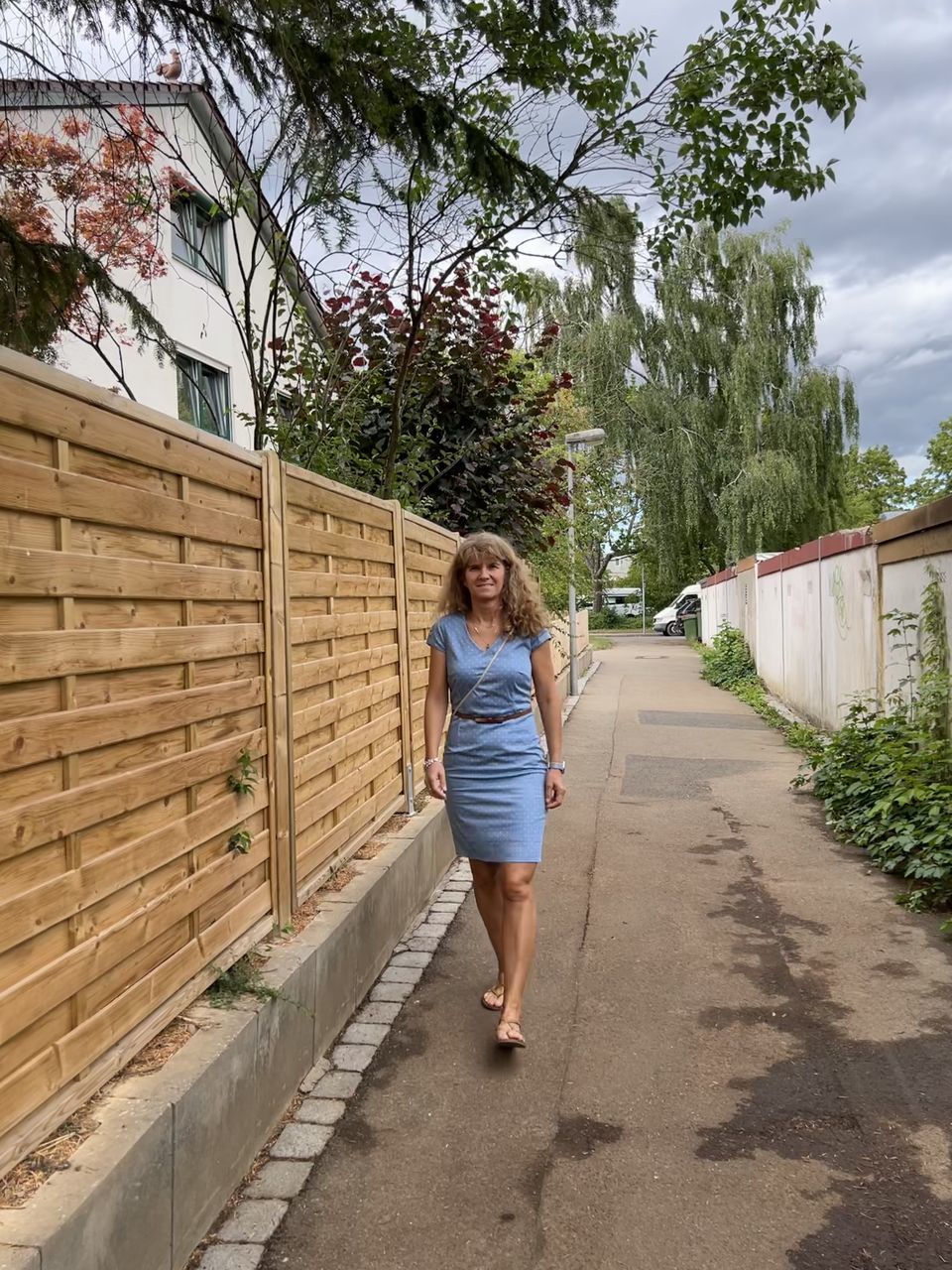 full length, one person, walkway, plant, adult, architecture, women, tree, lifestyles, leisure activity, casual clothing, nature, day, walking, young adult, footpath, built structure, wall, front view, hairstyle, standing, outdoors, female, city, sky, the way forward, clothing, building exterior, person, spring, smiling