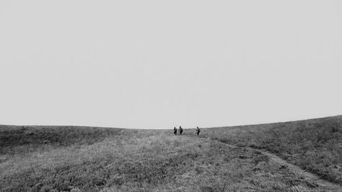 People walking on field against clear sky