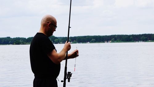 Bald man fishing in lake against sky