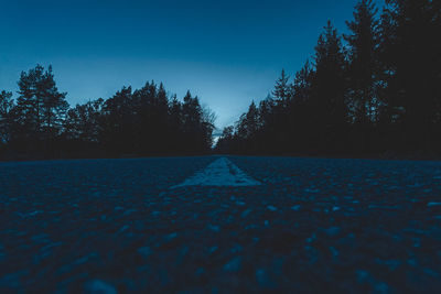 Surface level of road amidst trees against clear blue sky