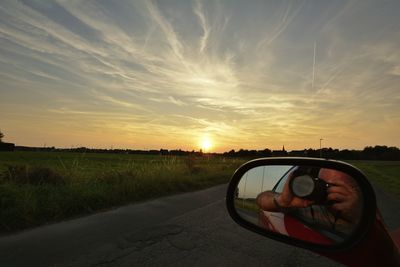 Man photographing car on road against sky during sunset