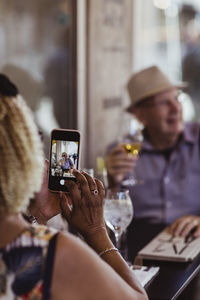 Cropped image of woman photographing man while sitting in cafe