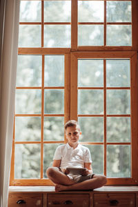 Full length of man sitting on table at window