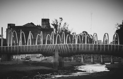 Bridge over river by abandoned building against clear sky