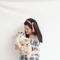 Young woman holding dog standing against white wall