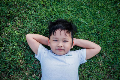 High angle portrait of cute boy lying on grassy field