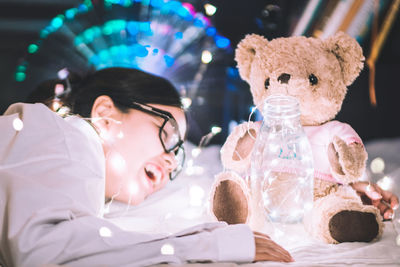 Close-up of girl with illuminated string light and teddy bear