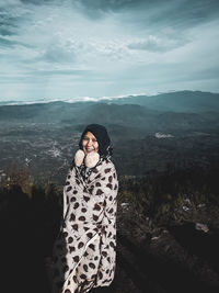 Portrait of young woman standing on mountain against sky