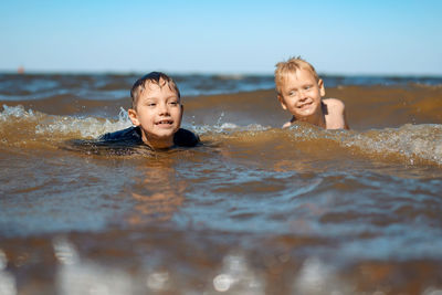 7-8 years old cute caucasian boys swimming in the sea with big splashes in waves