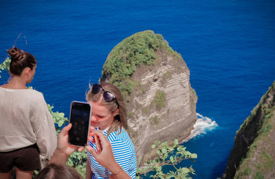 Young man photographing while using smart phone at sea