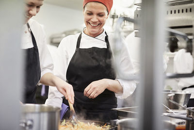 Teacher watching female chef student cooking food in kitchen at restaurant