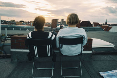 Rear view of people sitting on chair at sunset