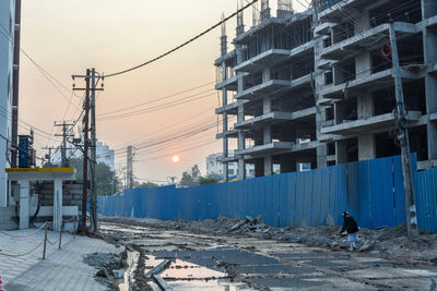 Construction site by buildings against sky during sunset