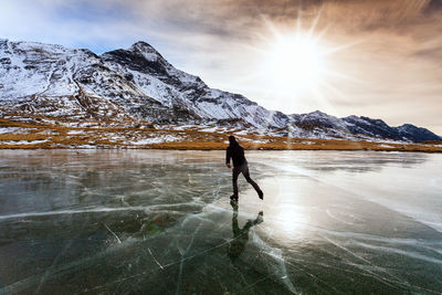 Woman walking on snowcapped mountain against sky during winter