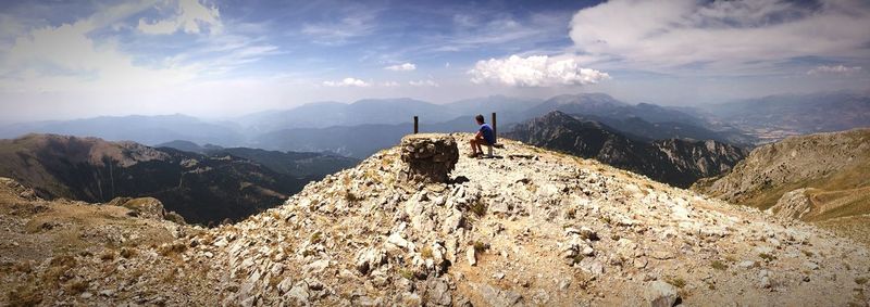 Side view of teenage boy looking at landscape while sitting on mountain against sky