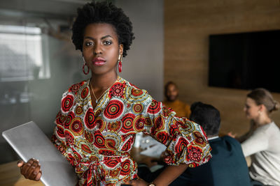 Portrait of beautiful woman holding camera while standing at home