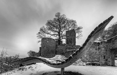 Bare tree by old building against sky during winter