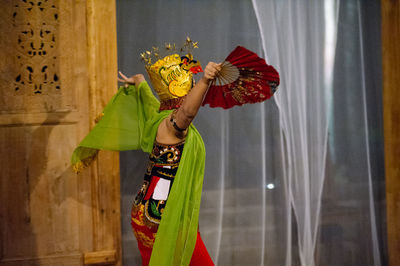 Side view of woman in traditional clothing performing dance by curtain