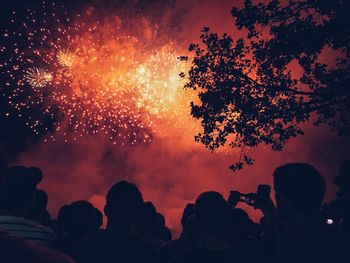 Low angle view of silhouette people looking at firework display in sky at night