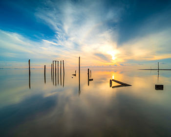 Silhouette wooden posts in sea against sky during sunset