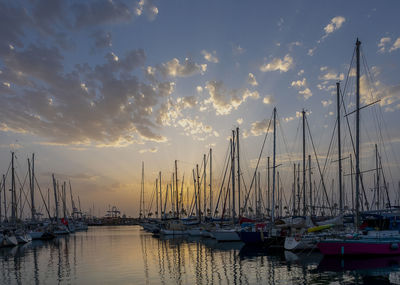 Sailboats moored in harbor at sunset