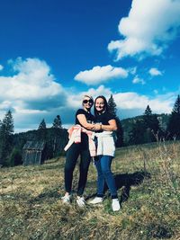 Portrait of smiling friends standing on grassy field against blue sky