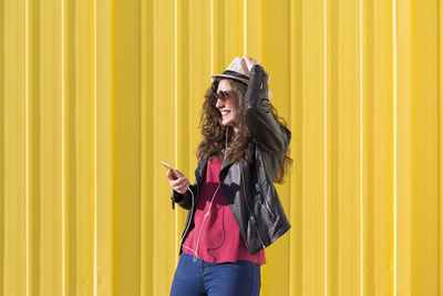 Woman holding umbrella standing against yellow wall