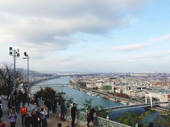 People standing at observation point by river against cloudy sky in city