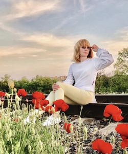 Girl sitting on rails in a field with poppies