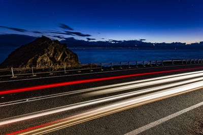 Light trails on road by sea against sky at night