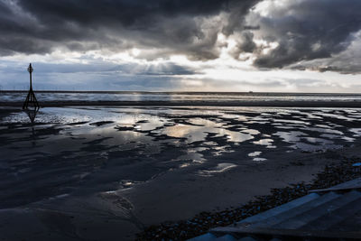 Silhouette pole at beach against cloudy sky